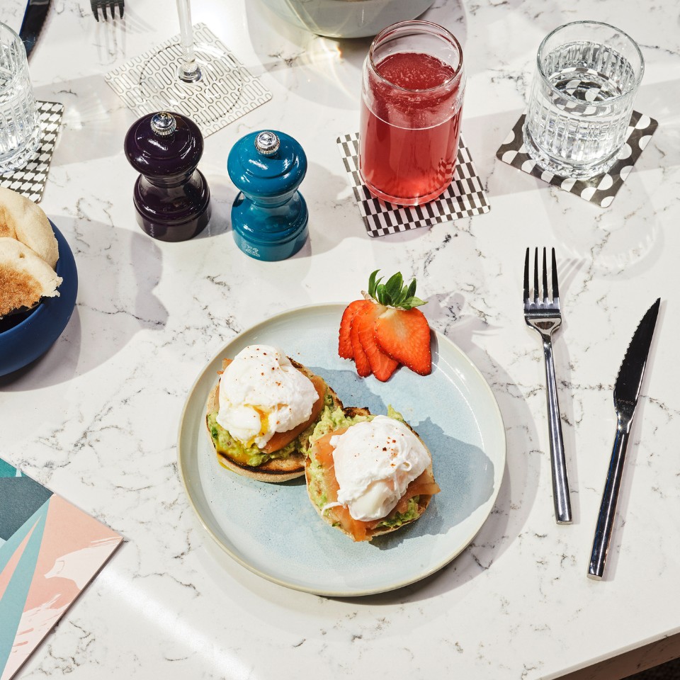 Avocado toast with salmon and an egg on a marble table, with drinks and cutlery
