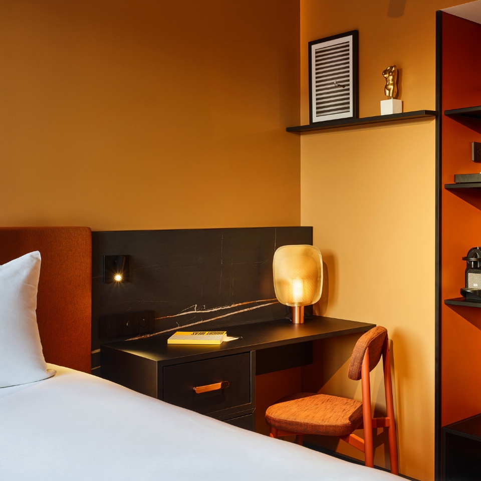 A small black desk with an orange chair next to a hotel bed