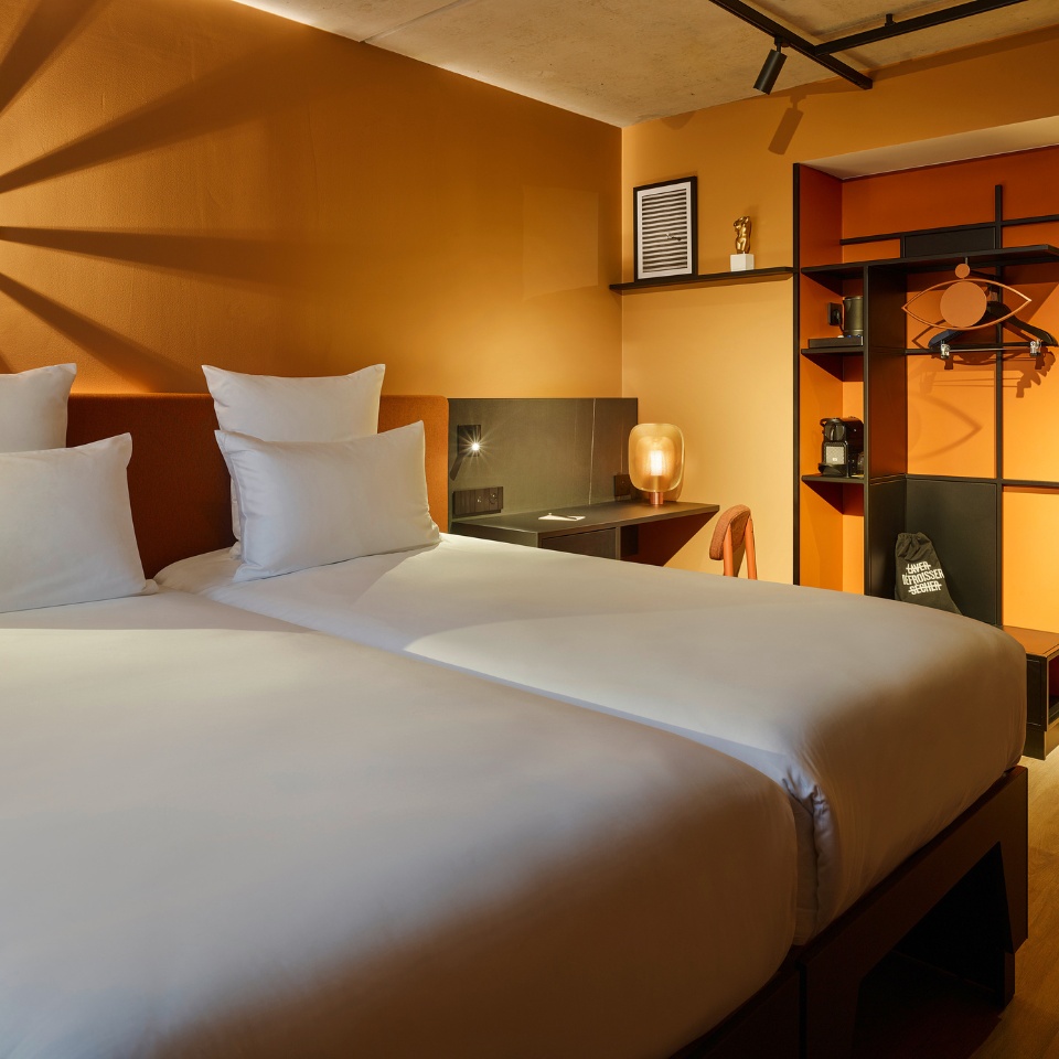 A twin bed with an orange headboard and a small black desk next to it, there is a black and orange wardrobe