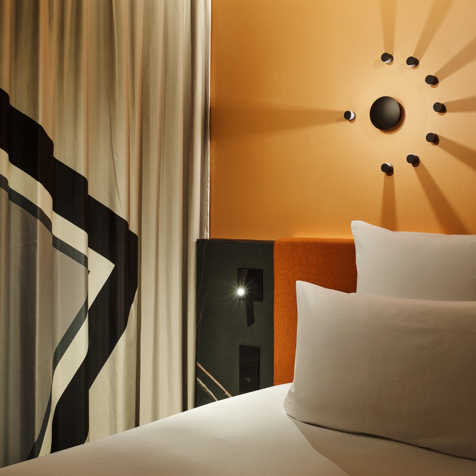 A close-up picture of a bed with two pillows on it, an orange headboard and a black lamp next to it