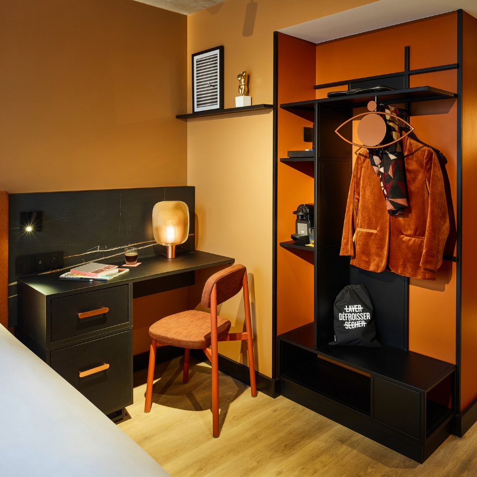 A small black desk with an orange chair and an orange-black wardrobe with a jacket in it