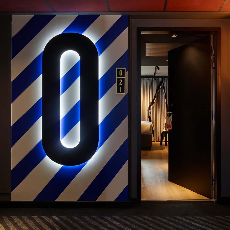 A black zero in front of a blue and white striped wall, it shows the floor number. in the background is an open door with a guest room