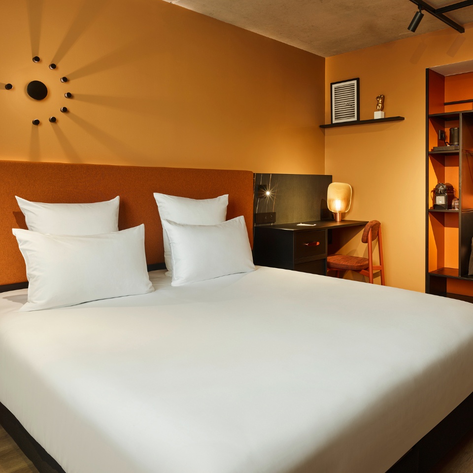 Guest Room with a double bed, small black desk and a wardrobe, the walls are orange