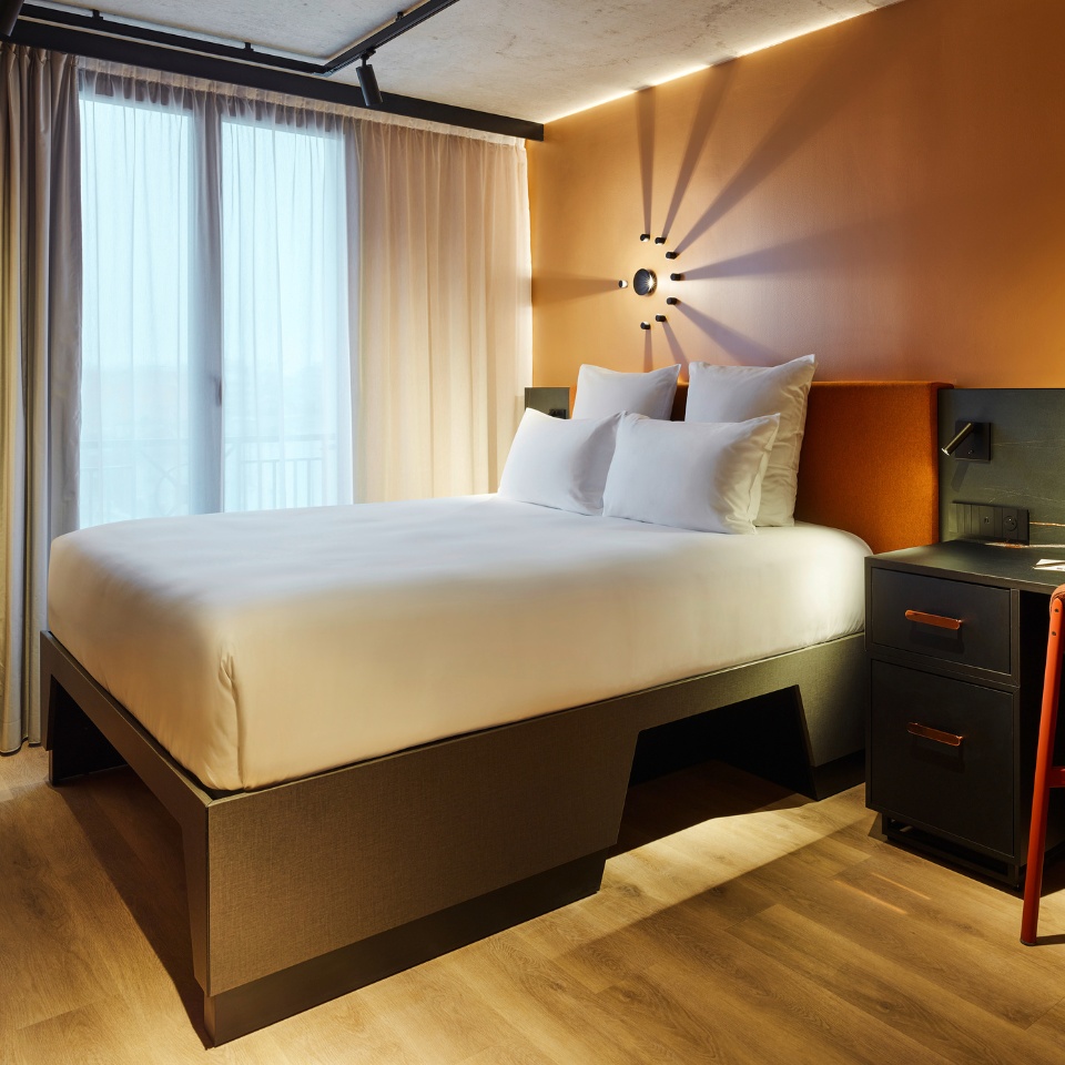 Guest Room with a double bed, small black desk and curtains, the walls are orange