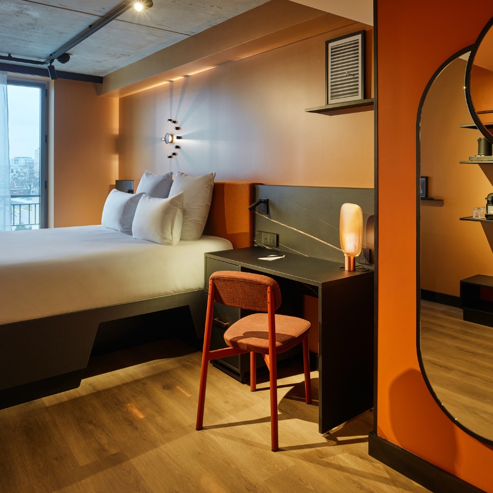 Guest Room with a double bed, small black desk and a mirror, the walls are orange
