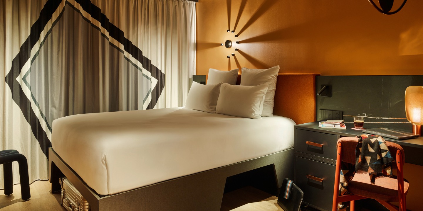 Double bed with an orange headboard and a small black desk next to it, the curtains are drawn