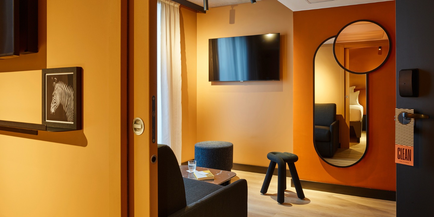 Living area in a hotel room with small black chairs and a couch and a marble coffeetable in front of a terrace door