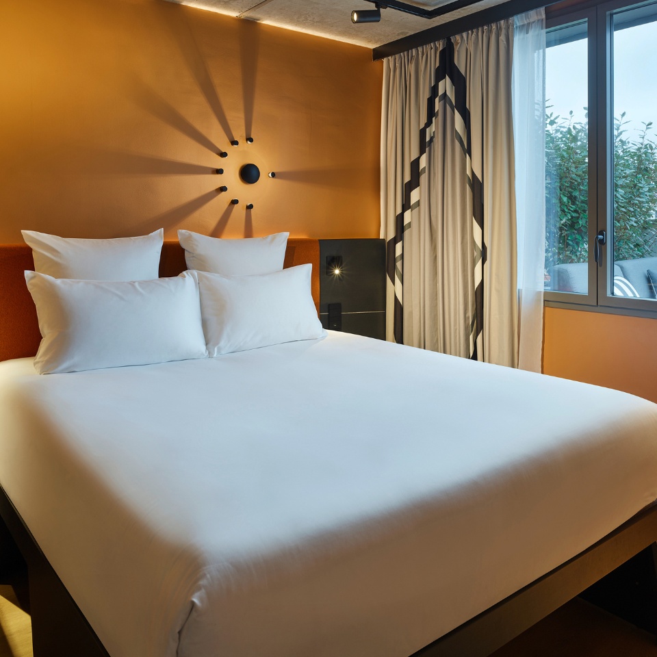 A double bed with an orange headboard next to a window with curtains