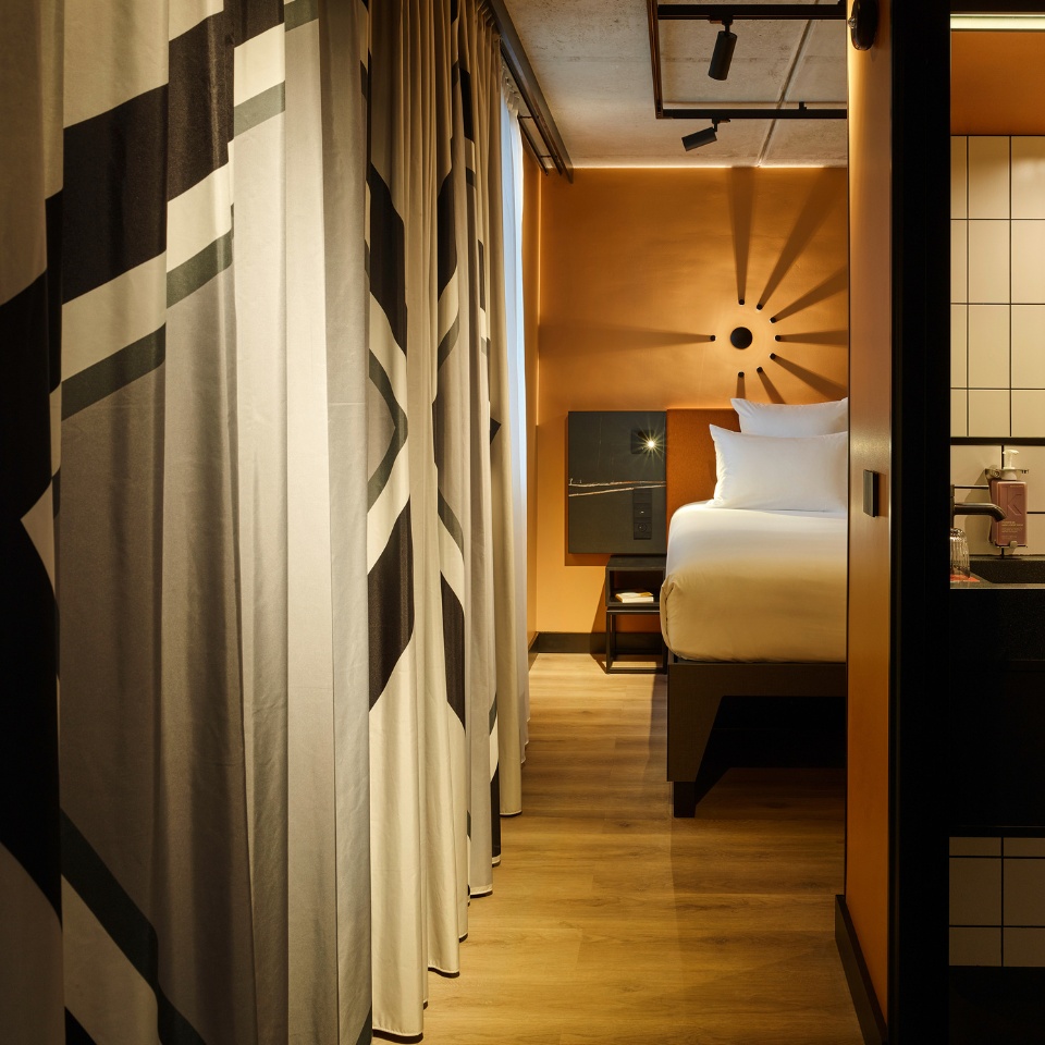 Double bed with an orange headboard and a small black desk next to it, the curtains are drawn