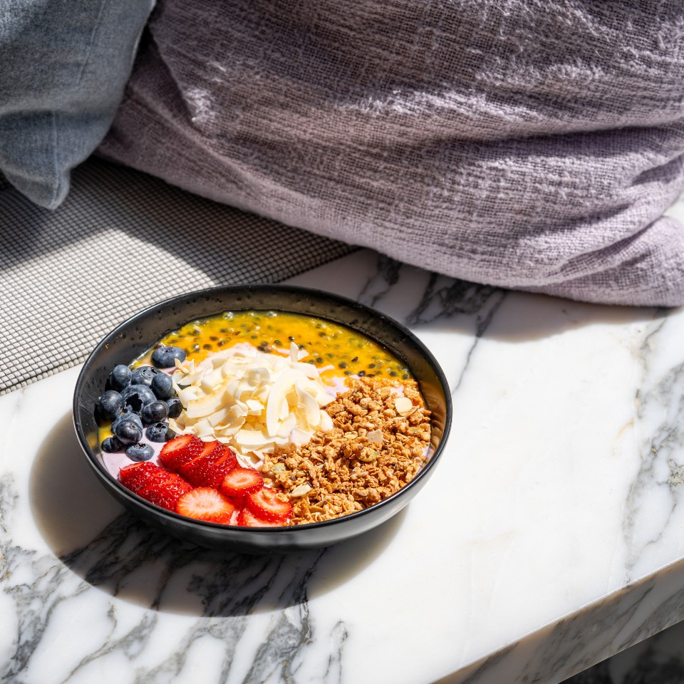Joghurt bowl on a counter. There are different toppings, such as strawberries, blueberries, granola, coconut flakes.