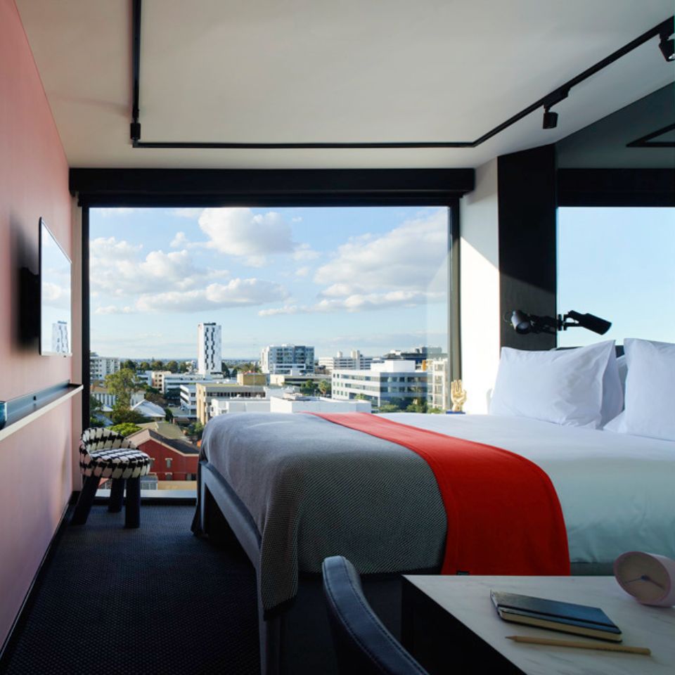 Guest room with a double bed, a small chair with a houndstooth pattern, a pink wall and floor to ceiling windows
