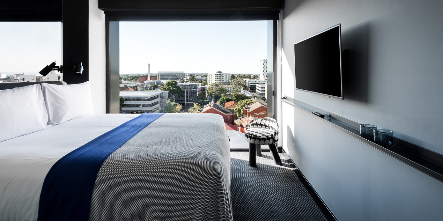 Guest room with a double bed, a small chair with a houndstooth pattern and floor to ceiling windows