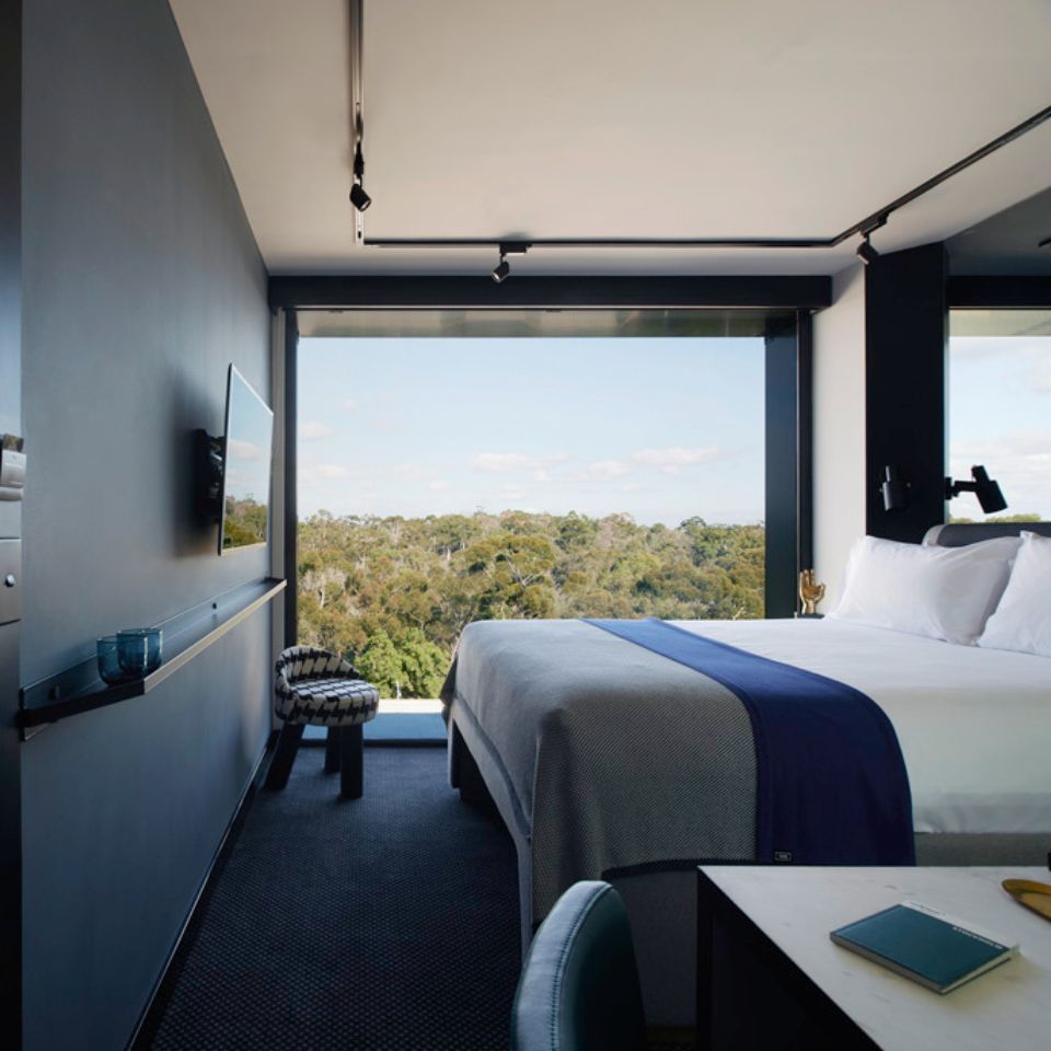 Guest room with a double bed, a small chair with a houndstooth pattern, a blue wall and floor to ceiling windows