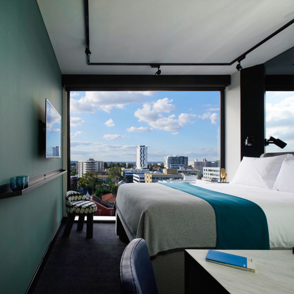 Guest room with a double bed, a small chair with a houndstooth pattern, a green wall and floor to ceiling windows
