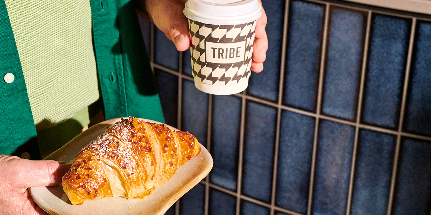 A person wearing a green shirt holding a cup of coffee and a croissant