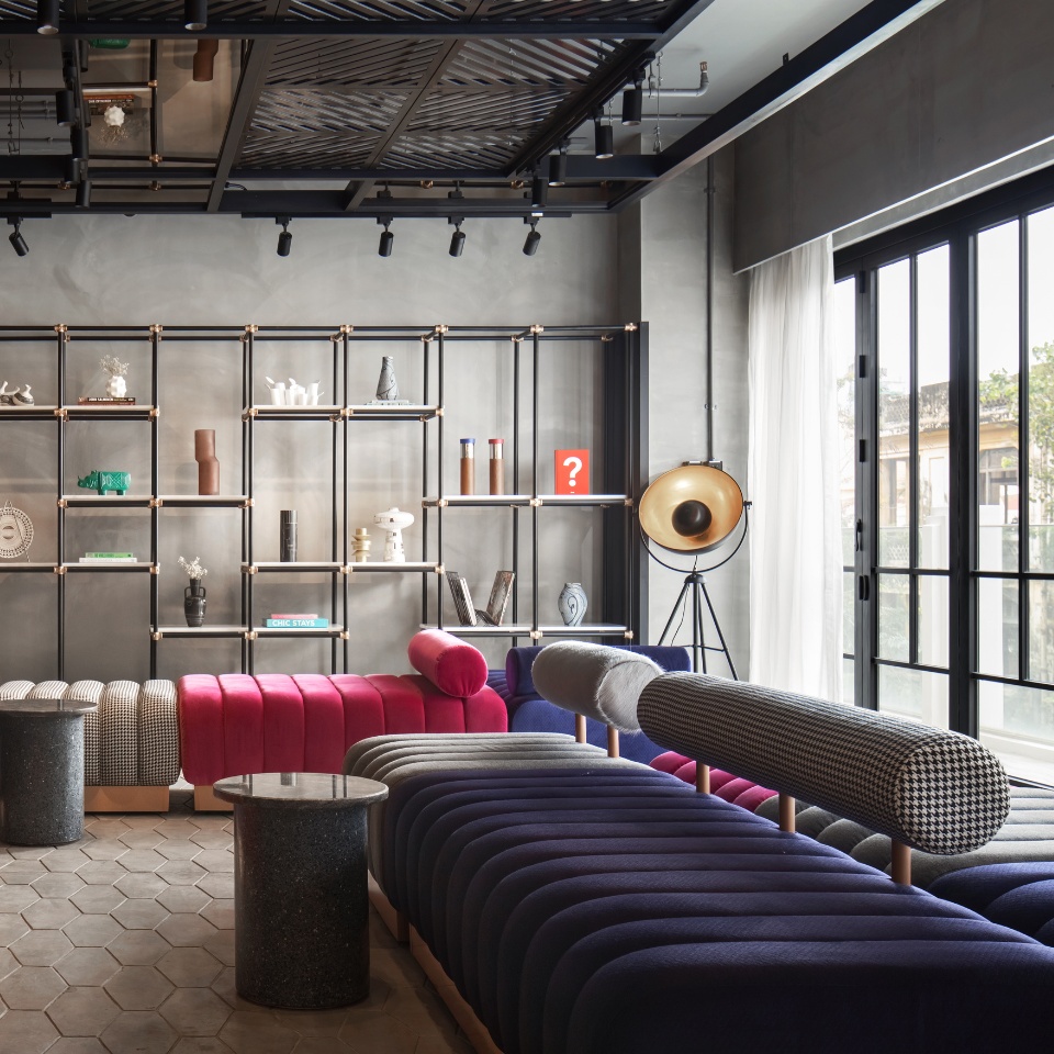 Pink, purple and grey couches with a big shelf with decoation on it in the background. there are floor-to-ceiling-windows