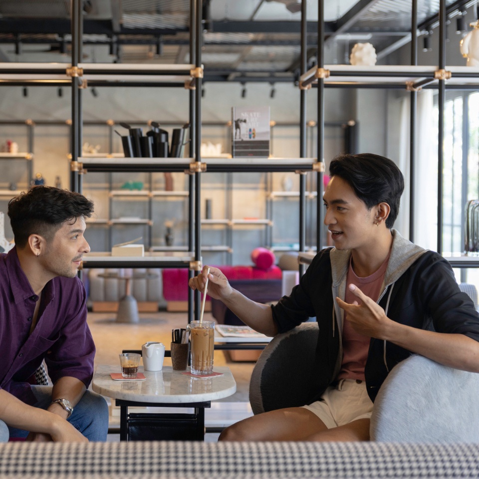 Two people sitting around a table, talking and drinking iced coffee