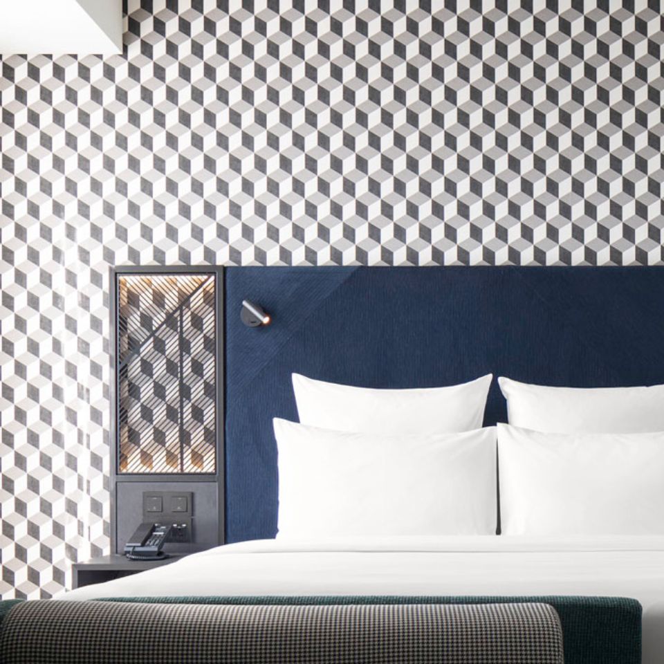 Double bed with white linens and a blue headboard in front of a patterned wall