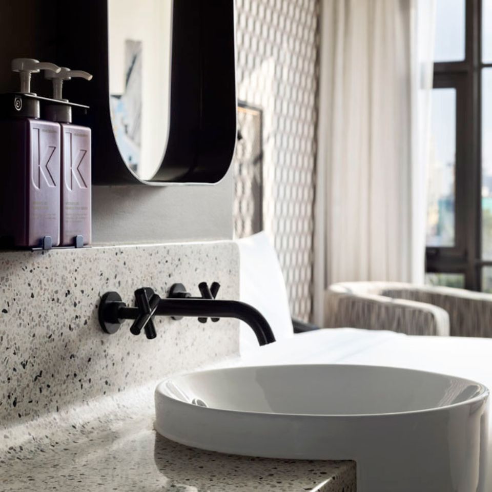 Washbasin with black faucets and two purple bottles of Kevin Murphy products on the left
