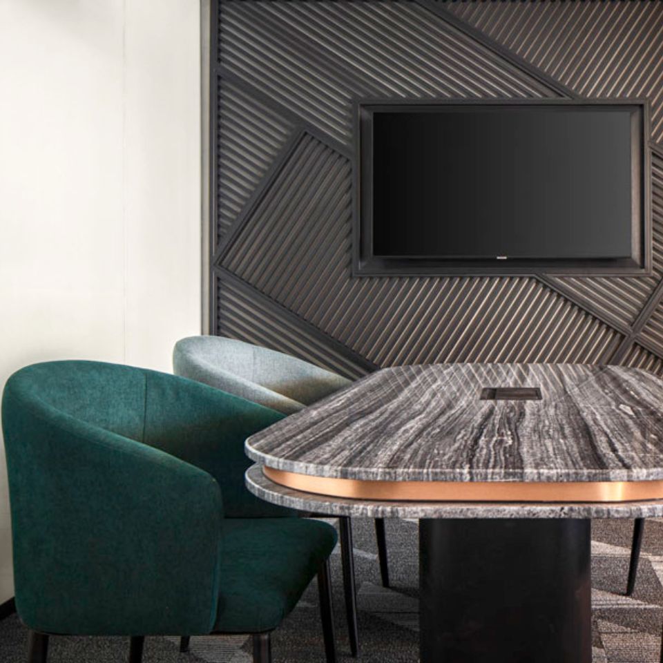 A meeting room with a marble table in the middle and two chairs next to it. There is a wall mounted TV.