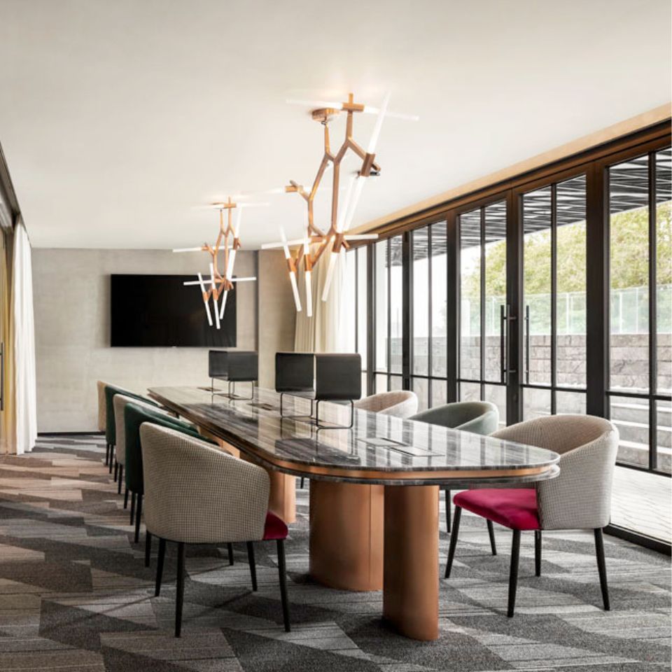 Armchairs in grey and green around a large table in a Co-Working area, next to a floor to ceiling window