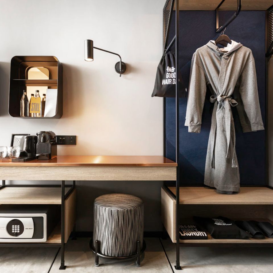 A wooden table with a coffee machine, a small shelf with water bottles and a wardrobe with a grey robe in it