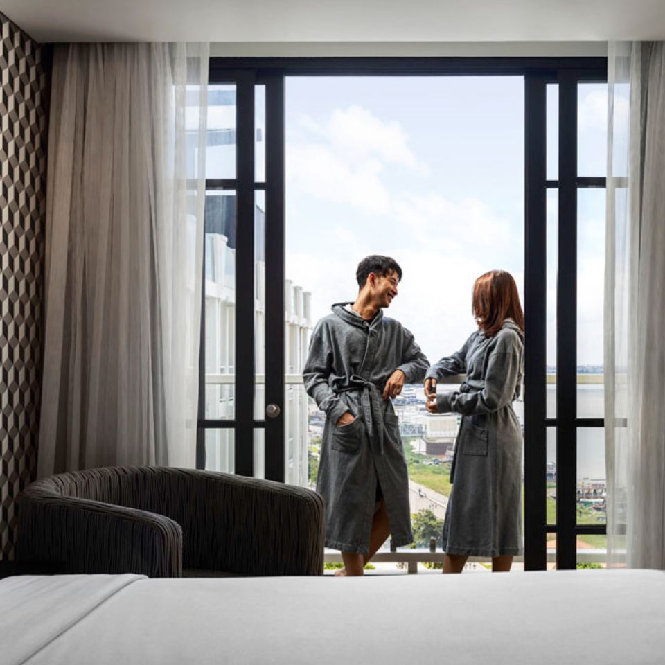 Two people in bathrobes standing on the balcony, engaging in conversation.