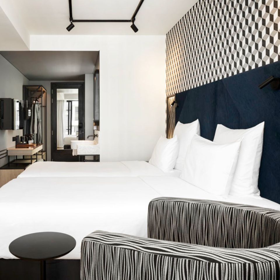 A grey armchair and a small black table, in the background is a double bed with a blue headboard