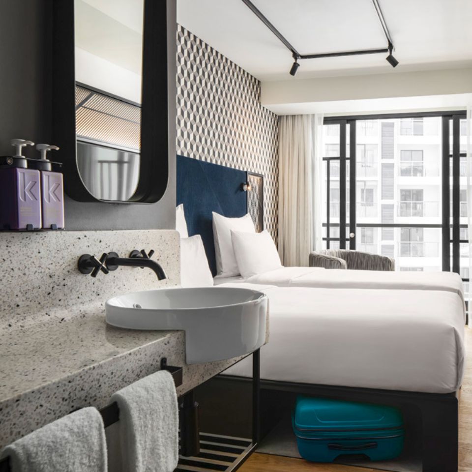 Guest room with a double bed, a blue headboard, an armchair and a washstand. The floor to ceiling window shows the city of Phnom Penh