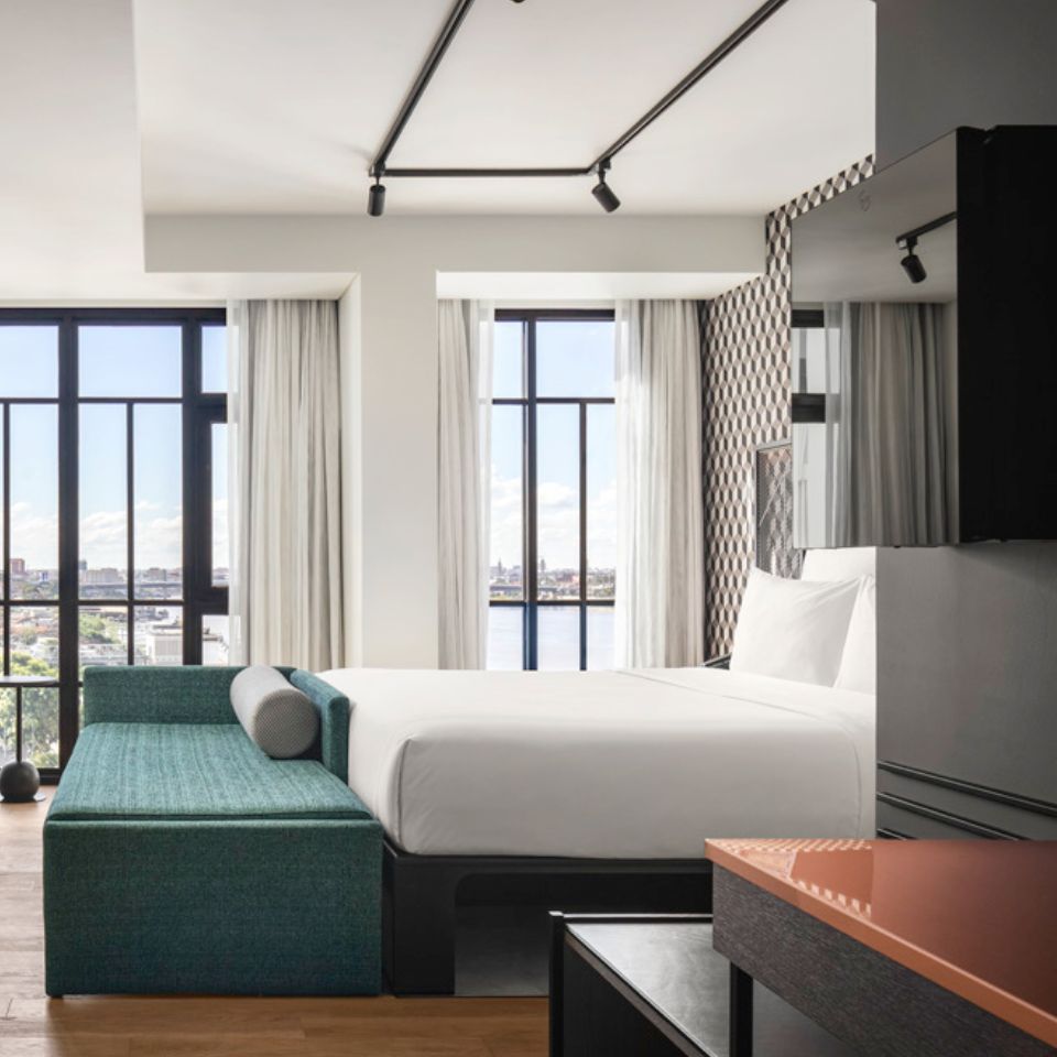 Guest room with a double bed, with a green seating unit at the end of the bed, an armchair and a washstand