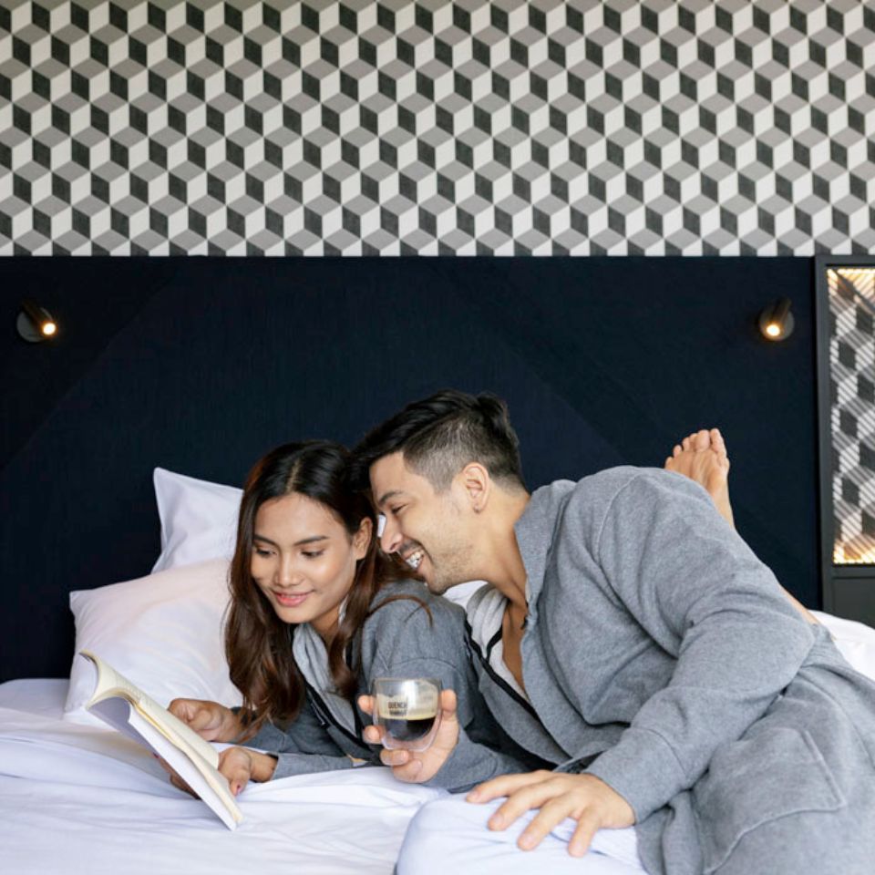 a happy couple wearing robes reading together looking at a book on a double bed