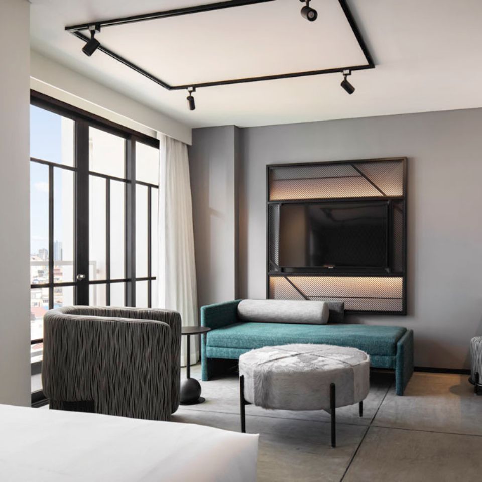 A grey armchair, a green seating unit and a small grey stool, on the wall is a black TV screen