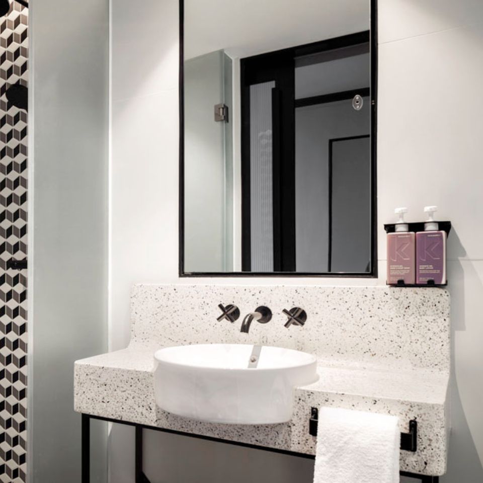 White washbasin with black faucet and a mirror, to the right are two purple bottles of Kevin Murphy products