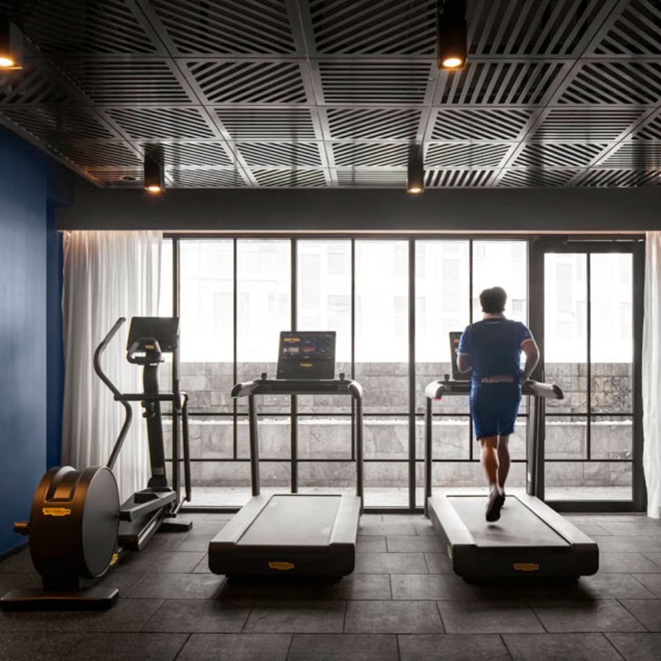 One fitness stepper and two treadmills in front of floor-to-ceiling window. a person is jogging on the right treadmill