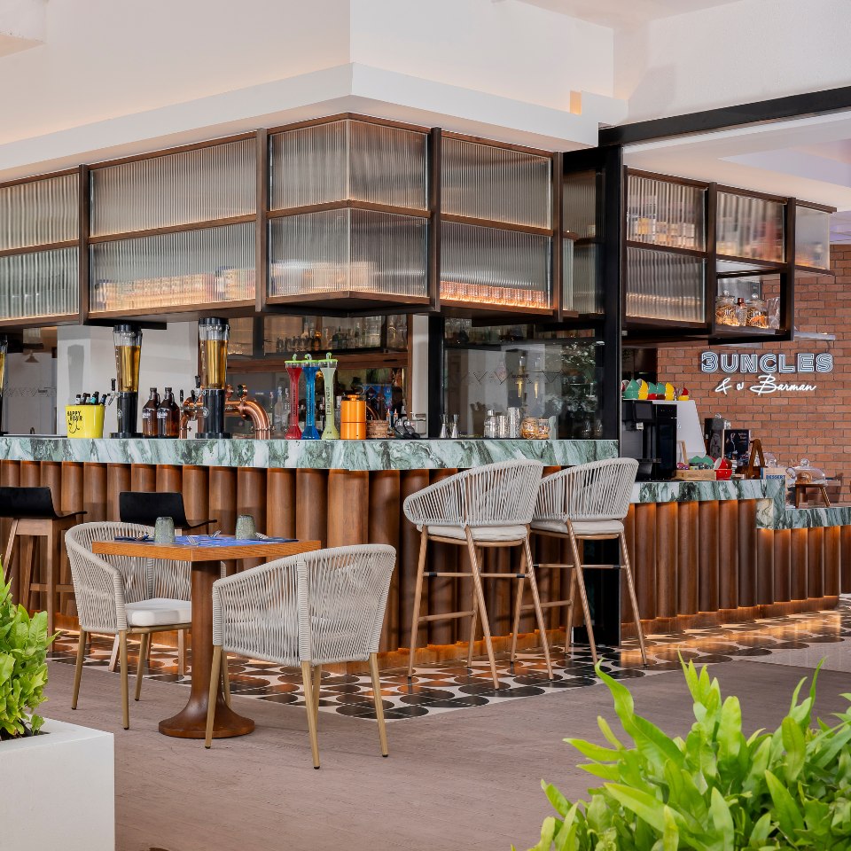 Stylish bar interior with a green marble countertop, wood accents, and wicker chairs. Warm lighting and lush greenery create an inviting atmosphere.