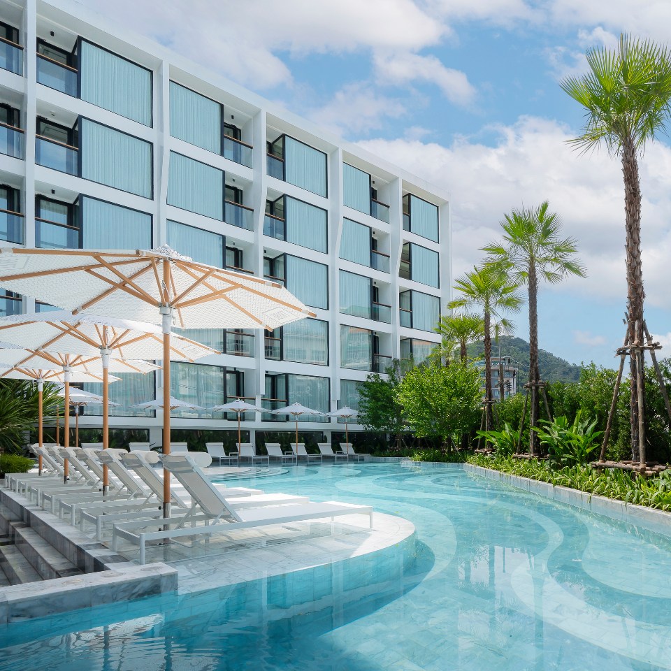 Modern hotel pool area featuring white lounge chairs, umbrellas, and palm trees, surrounded by a sleek, contemporary building.