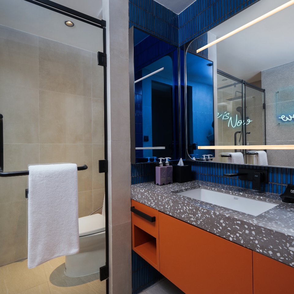Modern bathroom with sleek design. Features an orange vanity with terrazzo countertop, illuminated mirror, and a glass shower. Minimalistic and stylish.