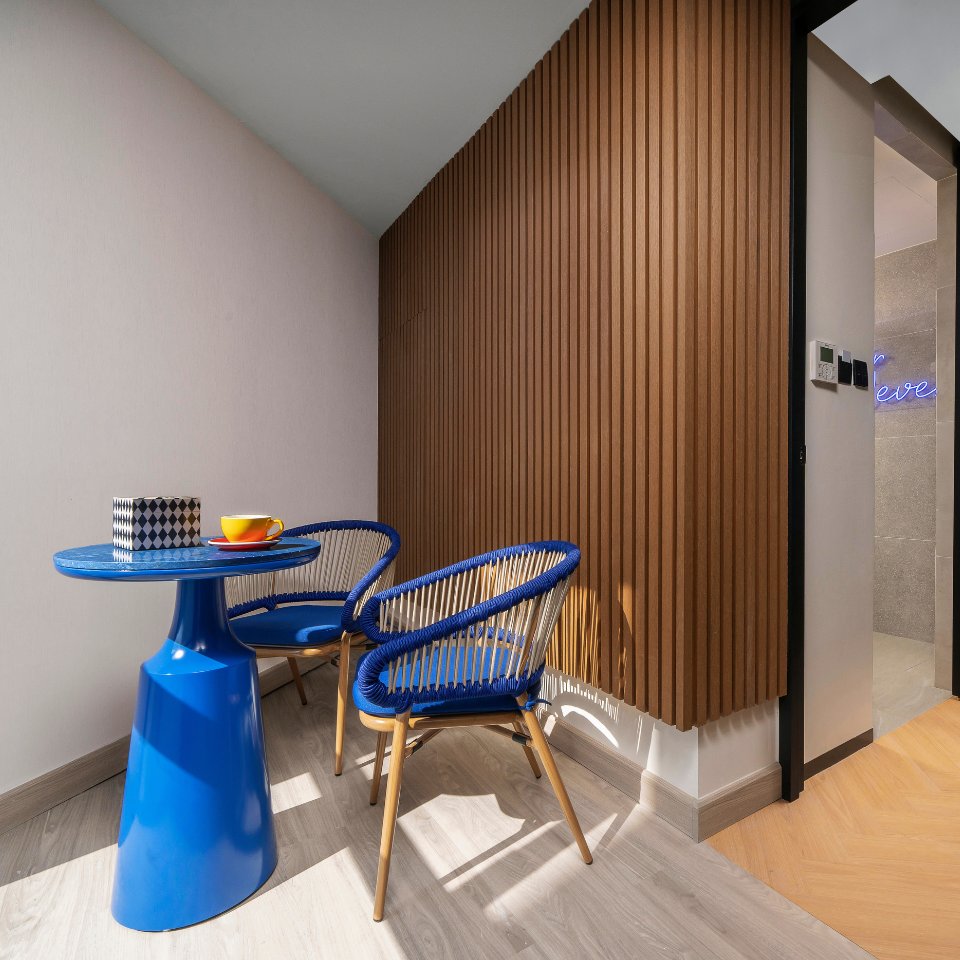 A cozy nook featuring a blue table, two stylish chairs, a box, and a colorful cup, set against a warm wooden wall.