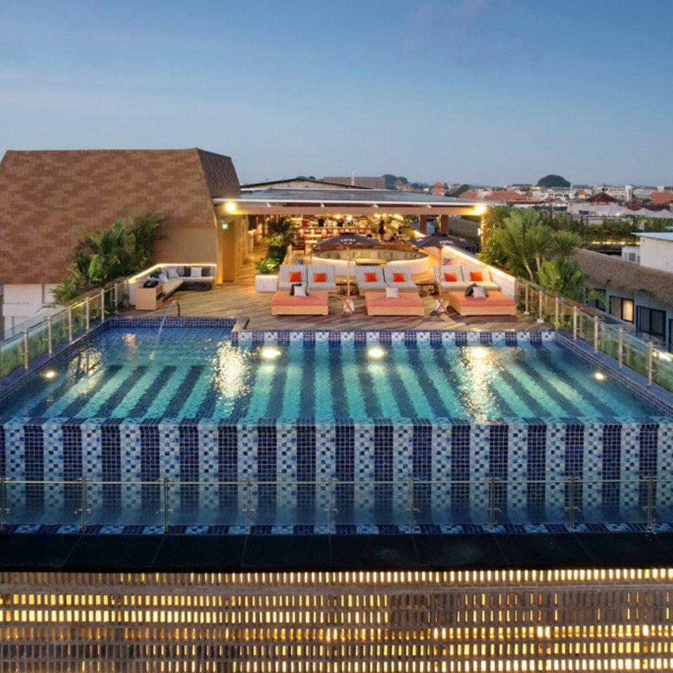 The rooftop pool and the lounge area with lounge chairs and umbrellas at TRIBE Bali Kuta Beach