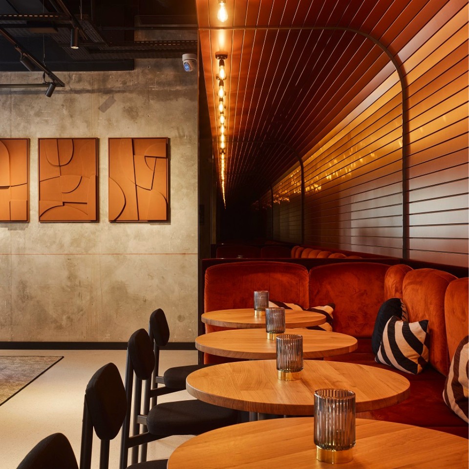 The social hub at TRIBE Saint Ouen with several round, wooden tables, black chairs and orange couches