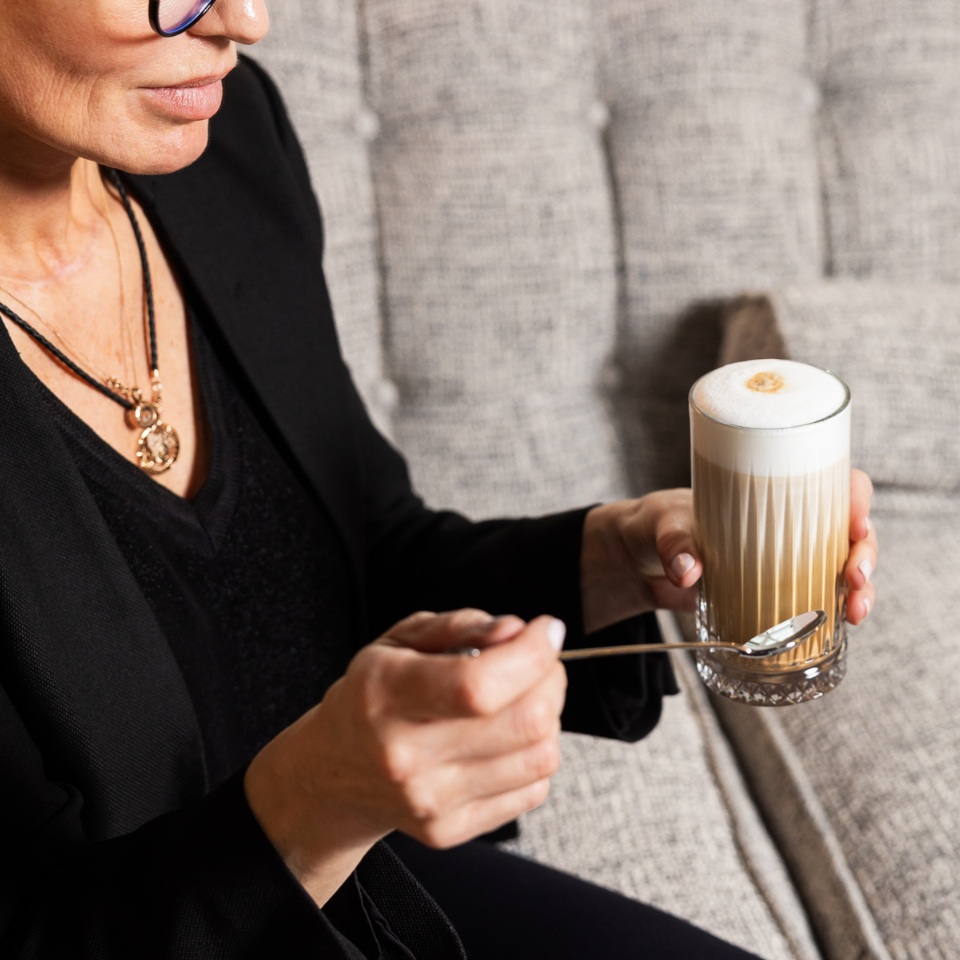 A woman is holding a coffee with milk in a glass