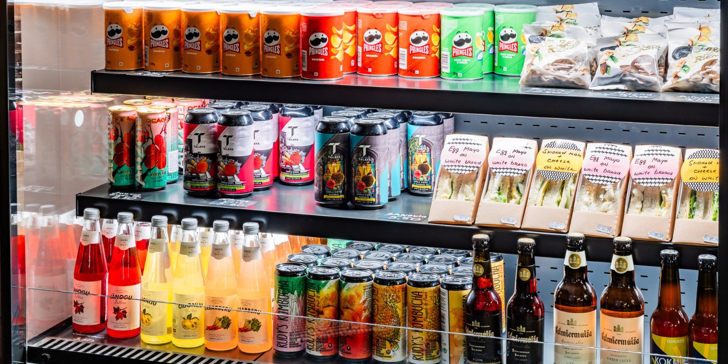 A display shelf filled with colorful beverage cans, Pringles, snacks, and sandwiches labeled with ingredients.