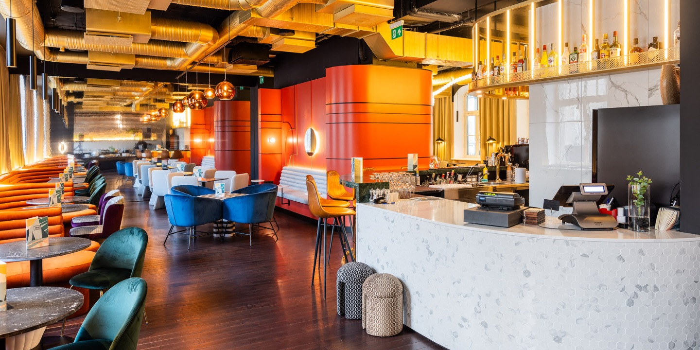 A modern hotel lobby featuring vibrant seating, a stylish bar, and elegant decor with warm lighting and lush textures.