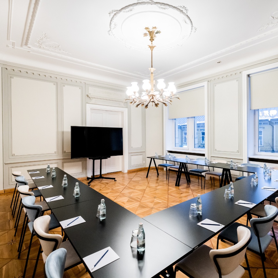 A stylish conference room with a chandelier, black tables arranged in a U-shape, and water bottles for a meeting.