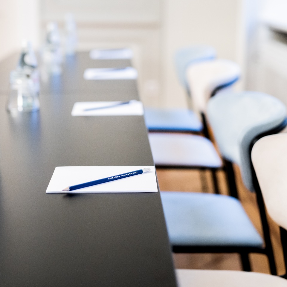 A conference table with water bottles, notepads, and a blue pencil, alongside stylish chairs, set for a meeting.