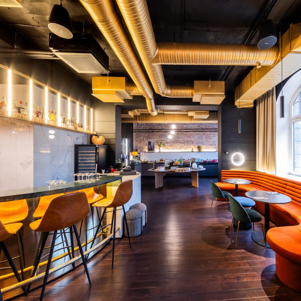 Modern restaurant and bar featuring curved orange booths, colorful chairs, and warm lighting along a wooden floor.