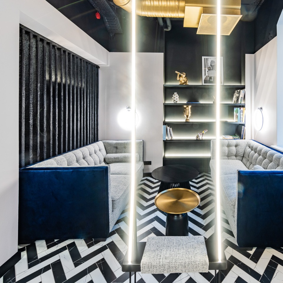 Lounge area with tufted gray sofas, a black coffee table, and sleek decor featuring shelves and modern lighting.