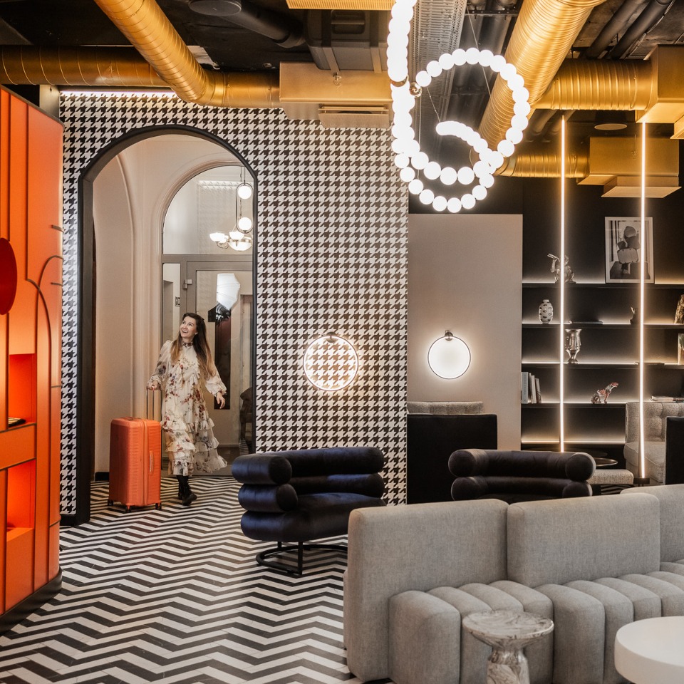 A stylish, modern lobby features a striking black and white houndstooth wall, sleek furniture, and an orange checkered suitcase.