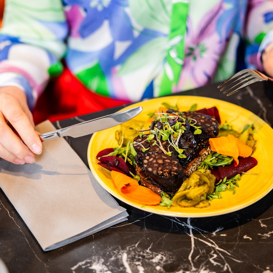 A colorful plate of blood pudding atop greens, garnished with sprouts and served with vibrant vegetables, ready to be enjoyed.