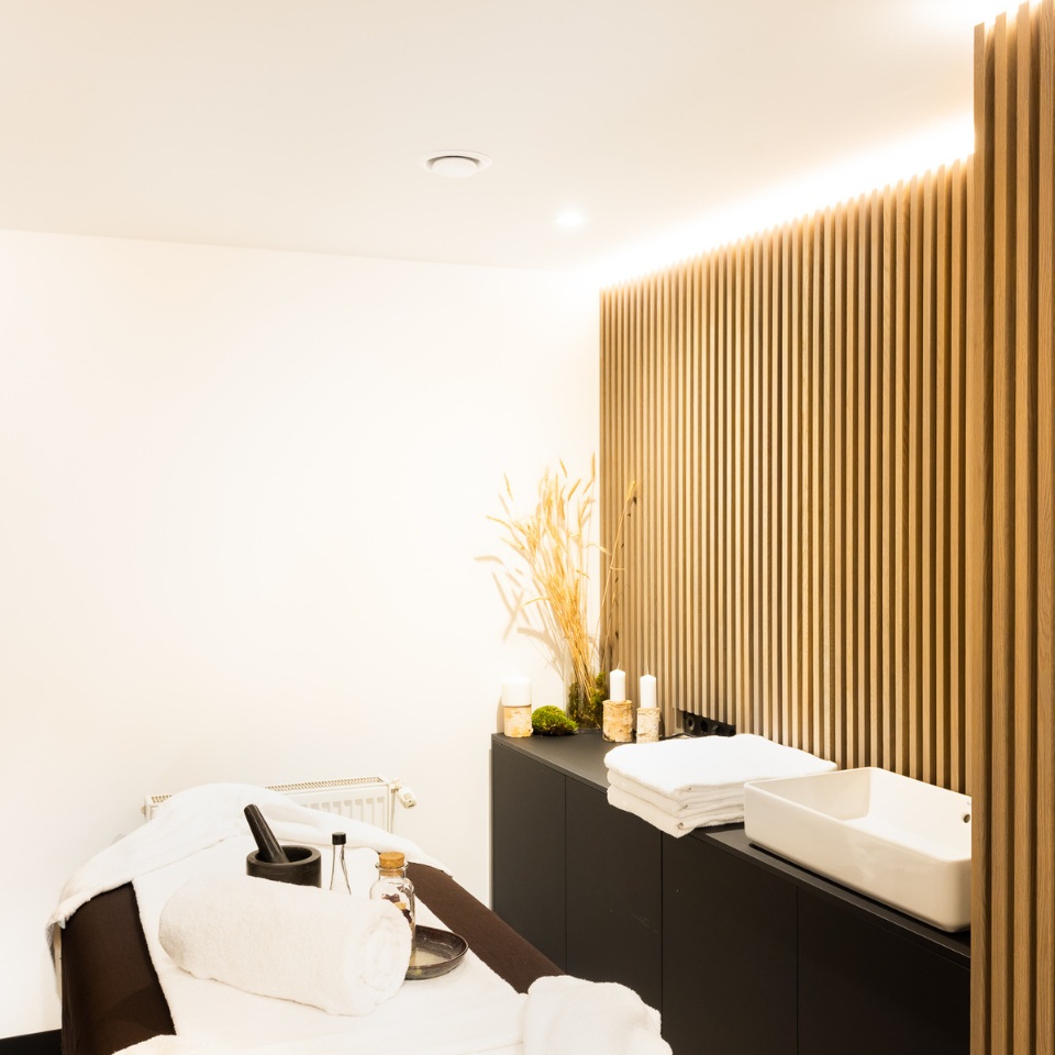 A serene spa room featuring a massage table with towels, a wooden accent wall, soothing candles, and decor for relaxation.